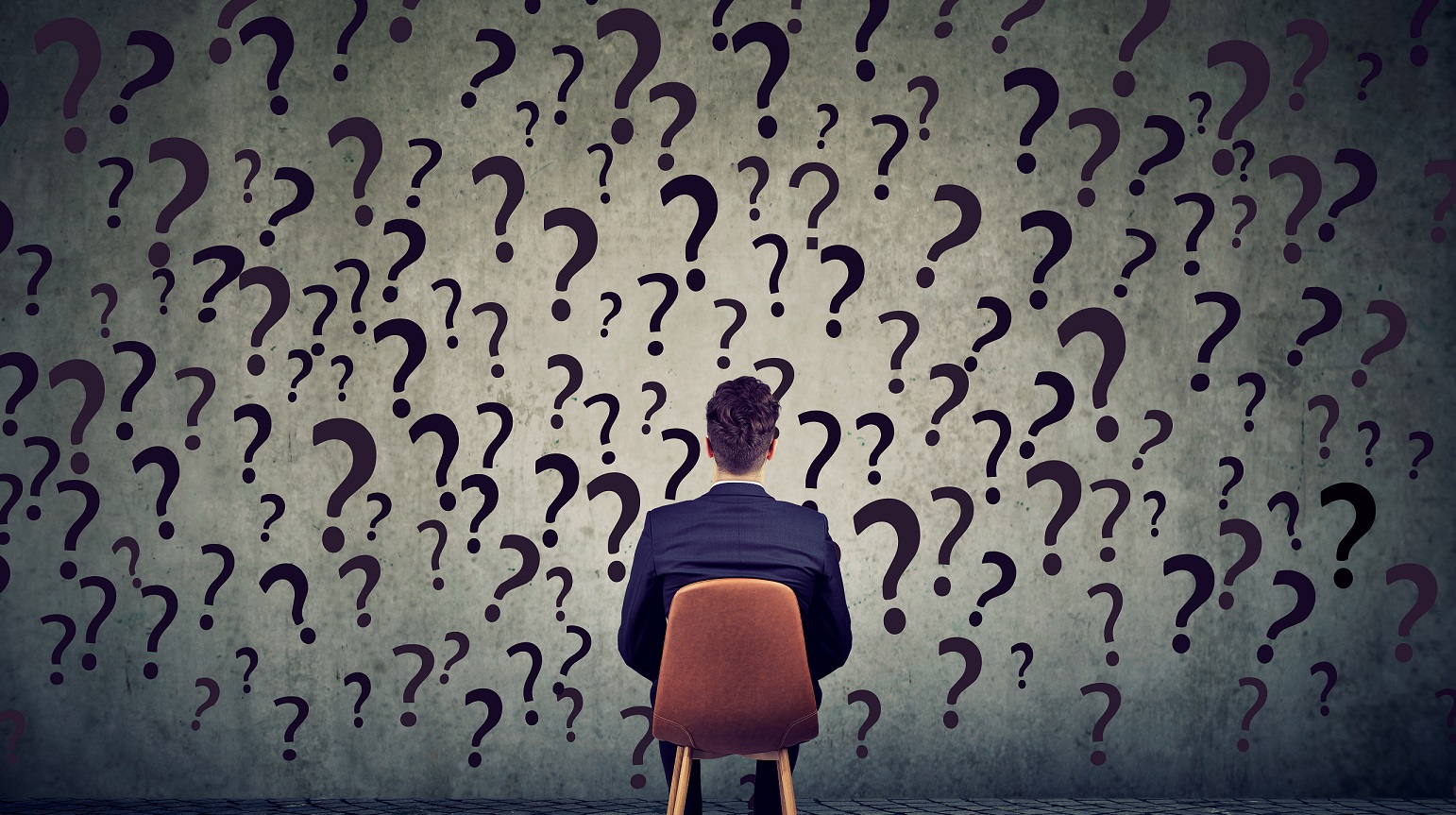 man sitting in front of a wall of question marks