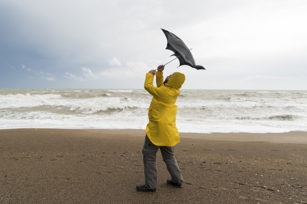 Homme sur une plage avec une veste de pluie jaune tenant son parapluie dans le vent